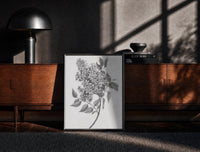Black-framed flowering lilac branch vintage art print print on a moody console with designer coffee-table books