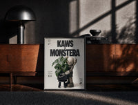 Black-framed KAWS Companion Monstera Nike framed poster print on a moody console with designer coffee-table books