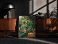 Black-framed garden with palm trees and figures vintage art print print on a moody console with designer coffee-table books