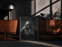 Black-framed elderly bearded man in shadow vintage art print print on a moody console with designer coffee-table books