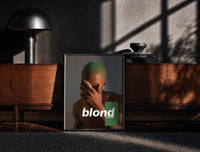 Black-framed Blond Frank Ocean Album Cover Portrait print on the floor in front of a dark wooden console