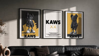 KAWS Monogram Impact triptych in three black frames on a grey wall above a leather sofa