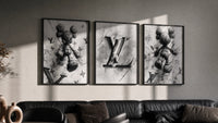 KAWS LV Monochrome Splash XX triptych in three black frames on a grey wall above a leather sofa