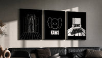 KAWS Monochrome Statement triptych in three black frames on a grey wall above a leather sofa