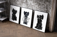 Blackout XX KAWS set of three black-framed prints leaning against a raw-plaster wall