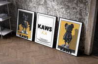 KAWS Monogram Impact set of three black-framed prints leaning against a raw-plaster wall