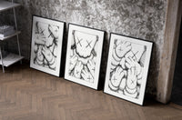 KAWS XX Crosshatch set of three black-framed prints leaning against a raw-plaster wall