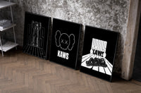 KAWS Monochrome Statement set of three black-framed prints leaning against a raw-plaster wall