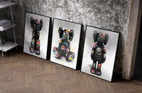 KAWS Companion Graffiti framed poster set of 3 set of three black-framed prints leaning against a raw-plaster wall
