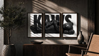 KAWS Monochrome Family triptych in three walnut frames above a sideboard in a warm room