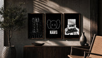 KAWS Monochrome Statement triptych in three walnut frames above a sideboard in a warm room