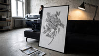 flowering lilac branch vintage art print print in a slim black frame leaning on a dark sofa in a concrete print studio