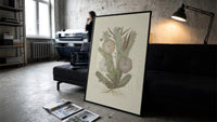 cactus with flowers vintage art print print in a slim black frame leaning on a dark sofa in a concrete print studio