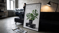 Nike Monstera Sneaker framed poster print in a slim black frame leaning on a dark sofa in a concrete print studio