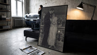 couple embracing on a night balcony vintage art print print in a slim black frame leaning on a dark sofa in a concrete…