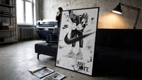 KAWS Companion Air Jordan Sneakers framed poster print in a slim black frame leaning on a dark sofa in a concrete print…