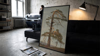 gnarled windblown pine tree against sky vintage art print print in a slim black frame leaning on a dark sofa in a…