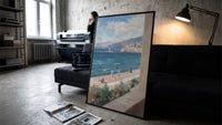 Mediterranean coastal promenade seen from balcony vintage art print print in a slim black frame leaning on a dark sofa in…