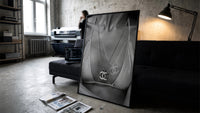 Chanel CC Necklace Black & White framed poster print in a slim black frame leaning on a dark sofa in a concrete print studio