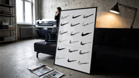 Nike Swoosh Hand-Drawn Sketch framed poster print in a slim black frame leaning on a dark sofa in a concrete print studio