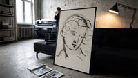 woman's head in flowing contour lines vintage art print print in a slim black frame leaning on a dark sofa in a concrete…