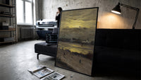 beach at sunset with silhouetted figures vintage art print print in a slim black frame leaning on a dark sofa in a…