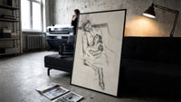 mother embracing seated daughter vintage art print print in a slim black frame leaning on a dark sofa in a concrete print…