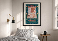 Jabon Hiel de Vaca La Giralda print in a black frame above a bed with striped linens, a brass wall lamp and a sunlit window