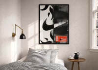 Nike Swoosh Streetwear print in a black frame above a bed with striped linens, a brass wall lamp and a sunlit window