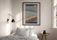 Hiroshige Sudden Shower Ohashi print in a black frame above a bed with striped linens, a brass wall lamp and a sunlit window