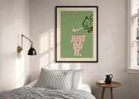 Just Do It Chameleon Green Pink print in a black frame above a bed with striped linens, a brass wall lamp and a sunlit window