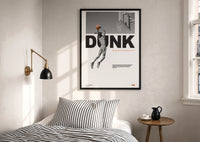 Basketball Dunk Motivation print in a black frame above a bed with striped linens, a brass wall lamp and a sunlit window