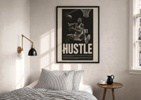 Dennis Rodman Hustle Basketball print in a black frame above a bed with striped linens, a brass wall lamp and a sunlit window