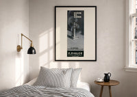 Crepe de Chine Millot Parfum print in a black frame above a bed with striped linens, a brass wall lamp and a sunlit window
