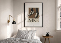 Nike Air Force 1 Streetwear print in a black frame above a bed with striped linens, a brass wall lamp and a sunlit window