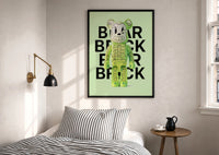 Green Glow Skeleton Bearbrick print in a black frame above a bed with striped linens, a brass wall lamp and a sunlit window