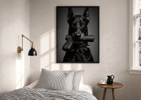 Doberman Pistol Spiked Collar print in a black frame above a bed with striped linens, a brass wall lamp and a sunlit window