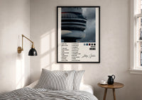 Drake Views CN Tower Tracklist print in a black frame above a bed with striped linens, a brass wall lamp and a sunlit window