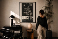 Dennis Rodman Hustle Basketball print in a black frame on a sunlit plaster wall, a person looking on beside a mushroom lamp