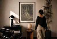 Dore Dante in the Dark Wood print in a black frame on a sunlit plaster wall, a woman looking on beside a mushroom lamp