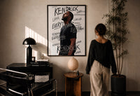 Kendrick Lamar Everything Profile print in a black frame on a sunlit plaster wall, a person looking on beside a mushroom lamp
