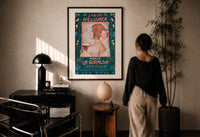 Jabon Hiel de Vaca La Giralda print in a black frame on a sunlit plaster wall, a woman looking on beside a mushroom lamp