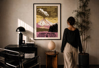 WPA Lassen Volcanic Park print in a black frame on a sunlit plaster wall, a woman looking on beside a mushroom lamp