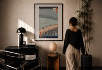 Hiroshige Sudden Shower Ohashi print in a black frame on a sunlit plaster wall, a woman looking on beside a mushroom lamp