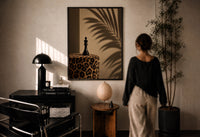 Leopard Print Chess King print in a black frame on a sunlit plaster wall, a person looking on beside a mushroom lamp