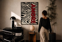 Amore Zebra Print in a black frame on a sunlit plaster wall, a person looking on beside a mushroom lamp