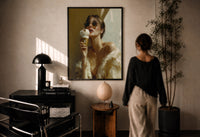 Louis Vuitton Gold Ice Cream print in a black frame on a sunlit plaster wall, a person looking on beside a mushroom lamp
