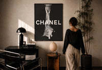 Chanel Black & White Luxury print in a black frame on a sunlit plaster wall, a person looking on beside a mushroom lamp