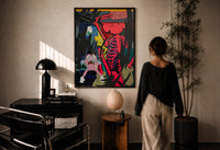 KAWS Down Time Skeleton Companion print in a black frame on a sunlit plaster wall, a person looking on beside a mushroom lamp