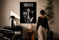Kurt Cobain Nirvana Live print in a black frame on a sunlit plaster wall, a person looking on beside a mushroom lamp